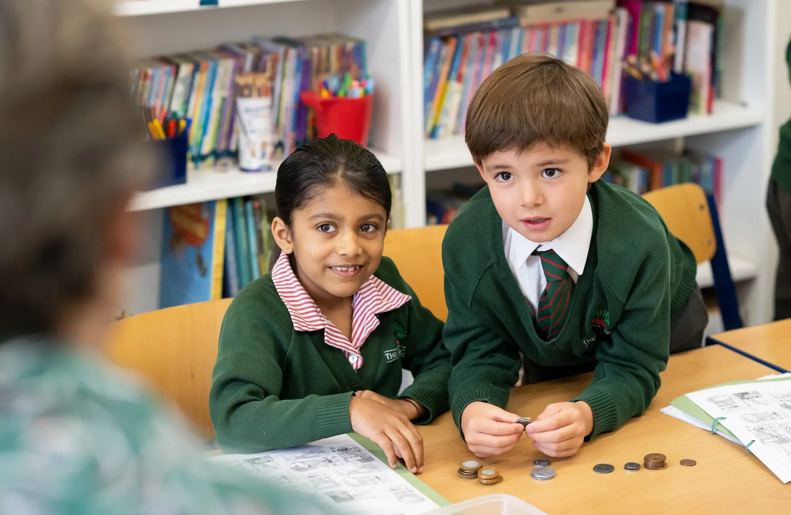 Two students sitting together at a table with bookshelves in the background