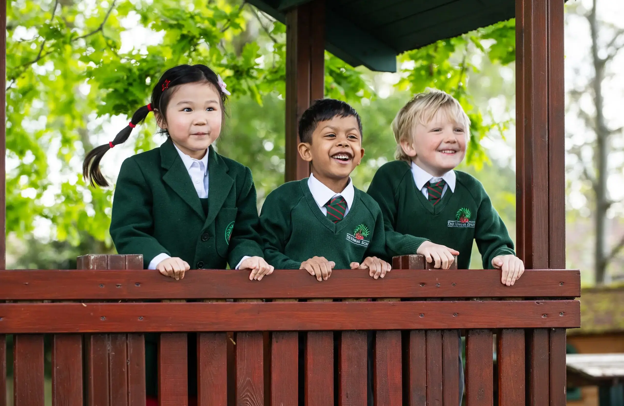 Three students looking out from a wooden playground structure