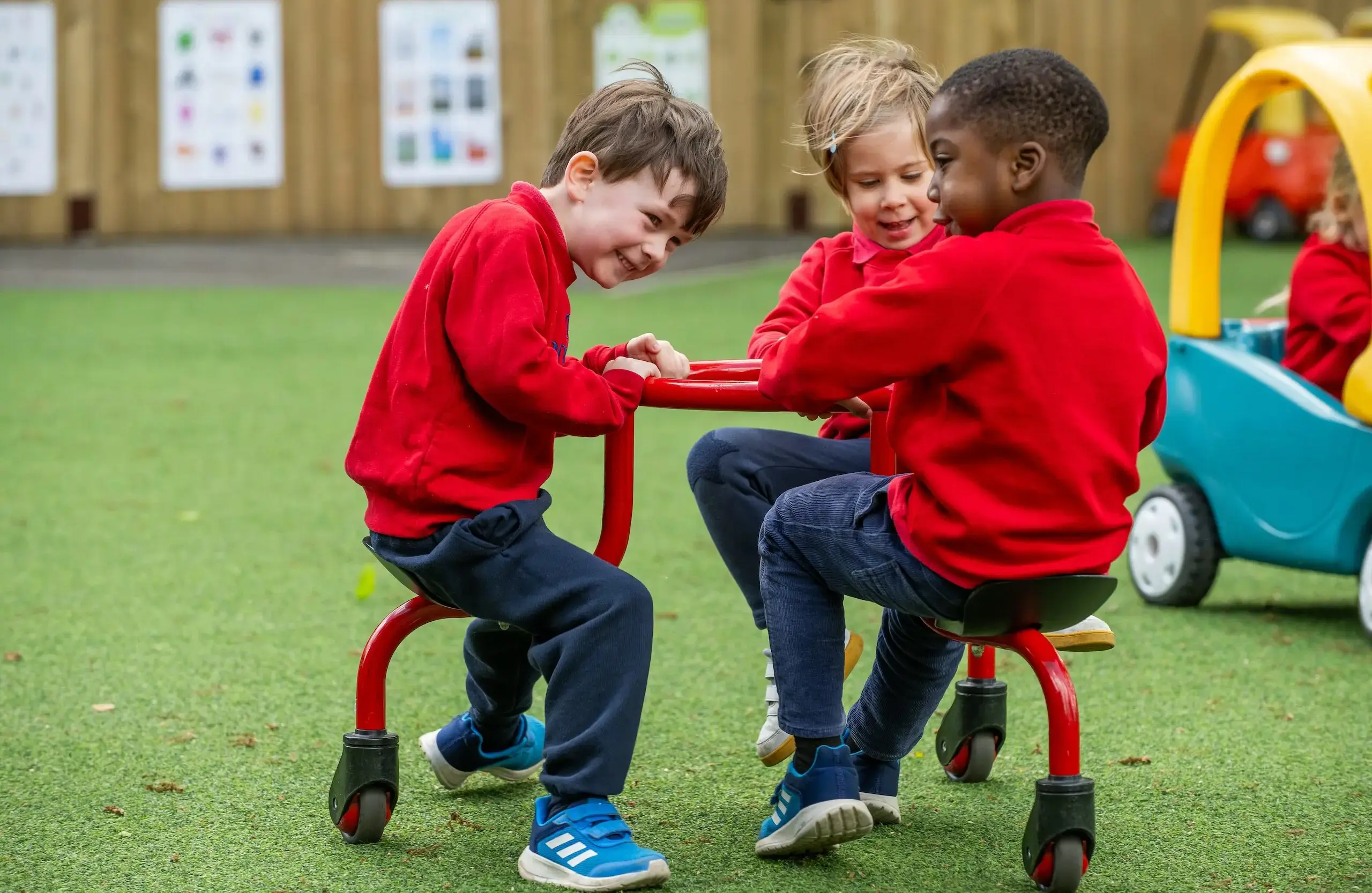 Three students in red jumpers sitting on playground equipment