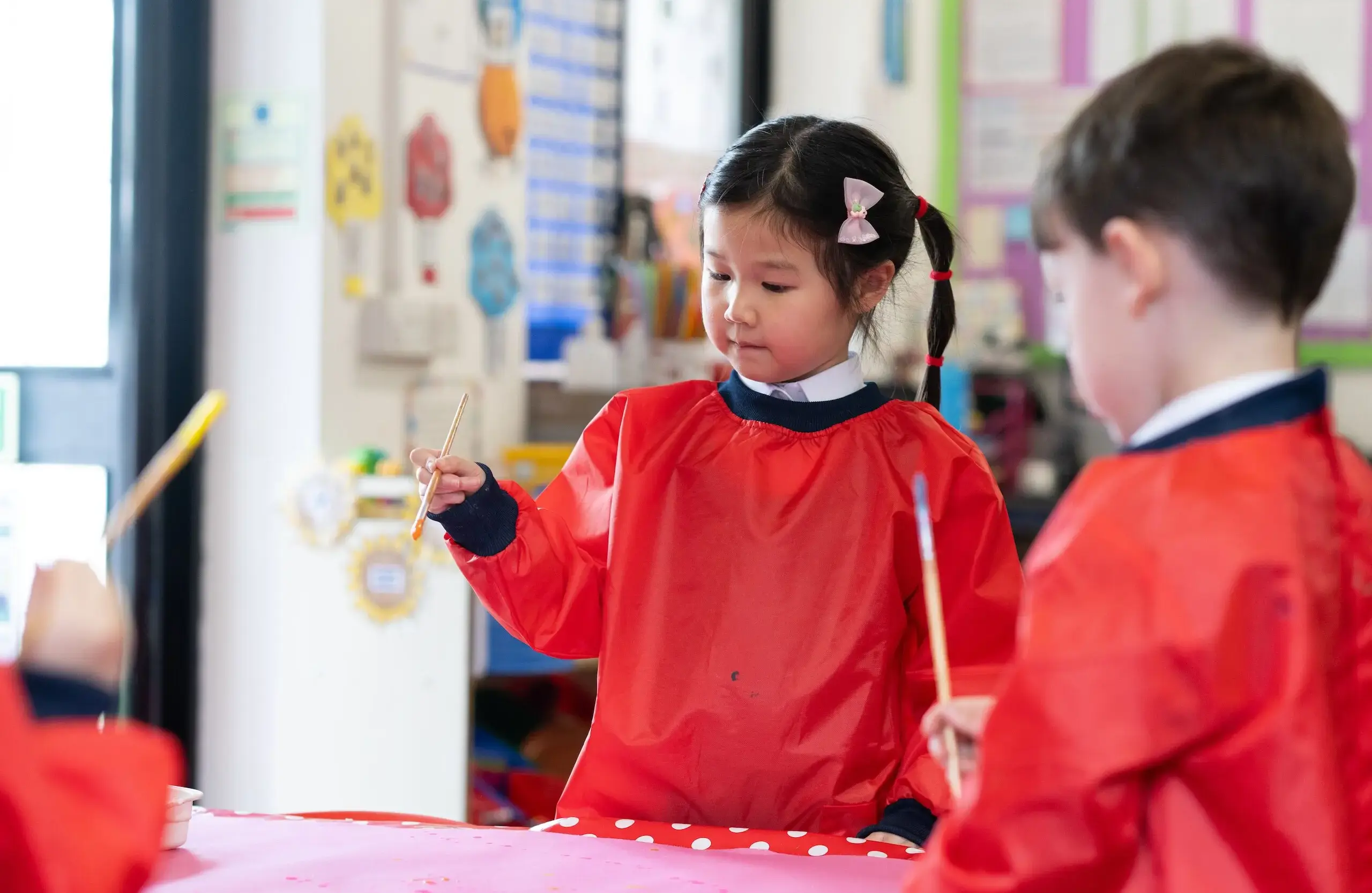 Schoolchildren wearing protective paint covers and painting