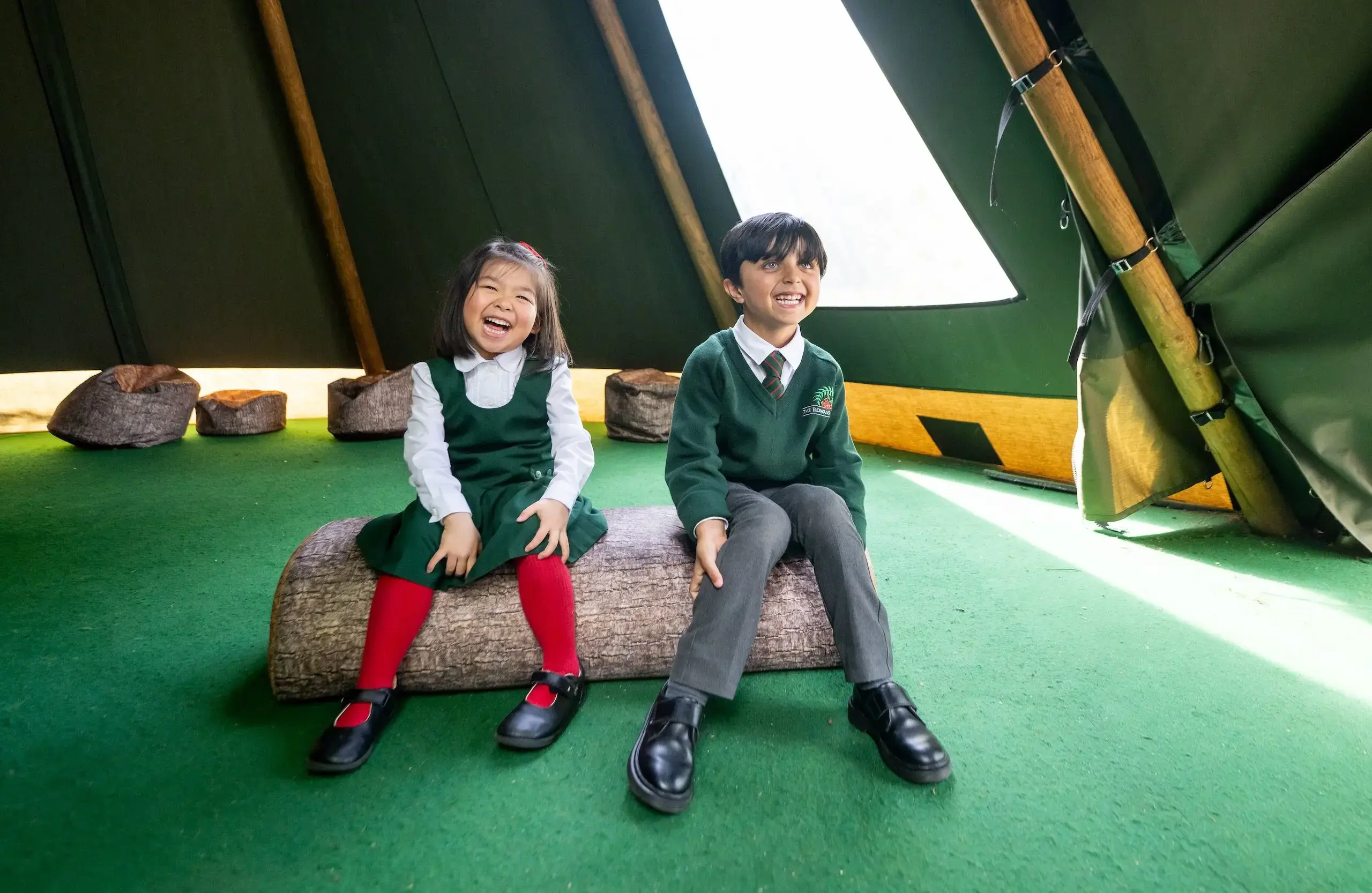 Two children sitting on a log in a teepee, laughing