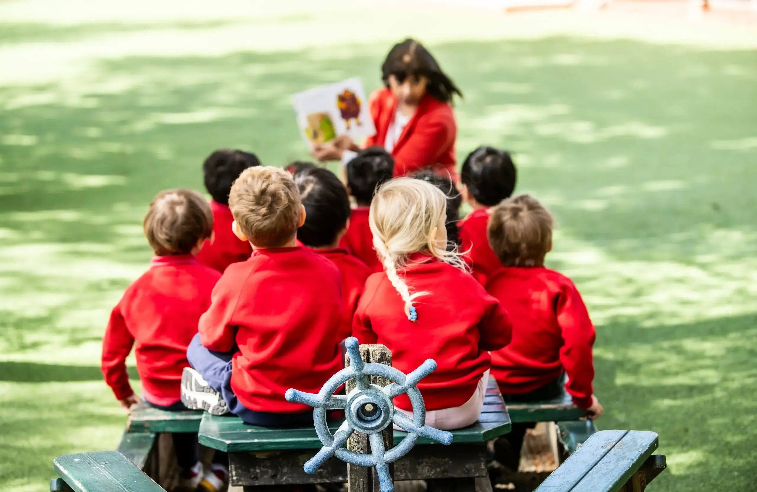 Students sitting on a nautical-themed picnic bench listening to their teacher