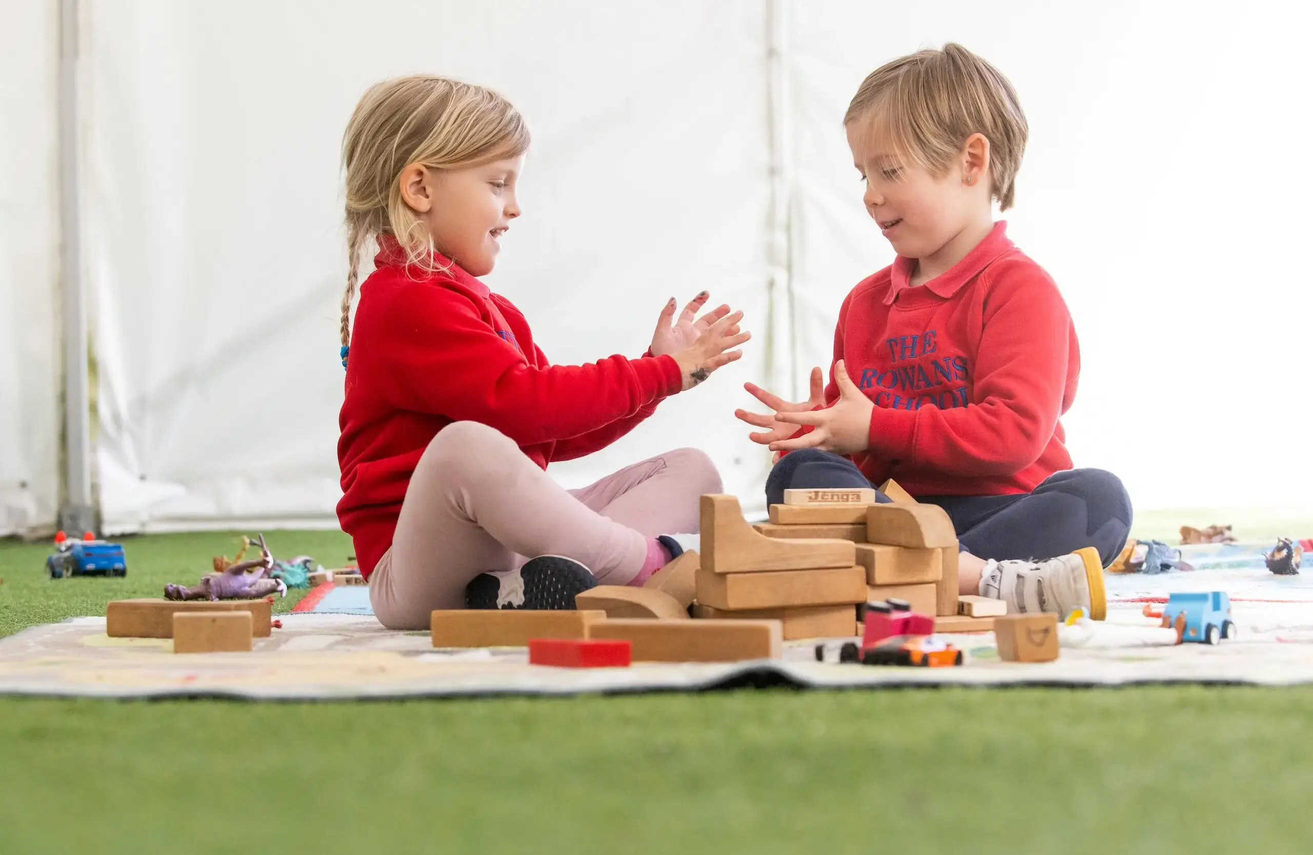Two young students playing with wooden blocks, sitting cross-legged on a mat