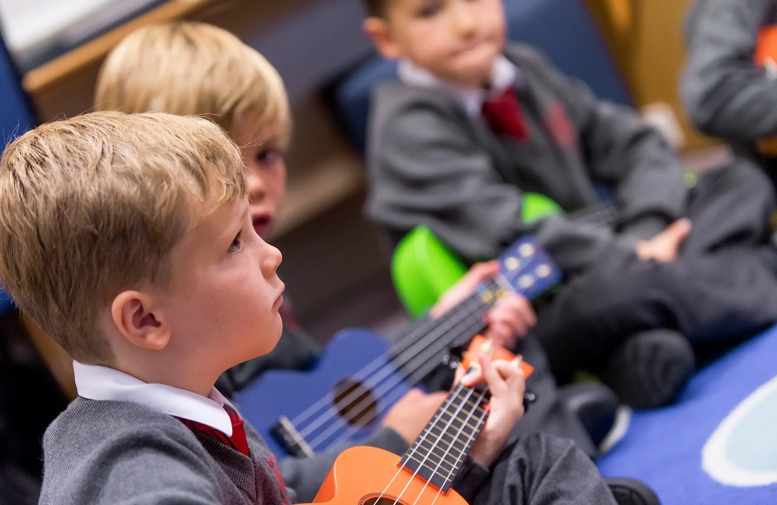 Students sitting cross-legged on a carpet, playing instruments