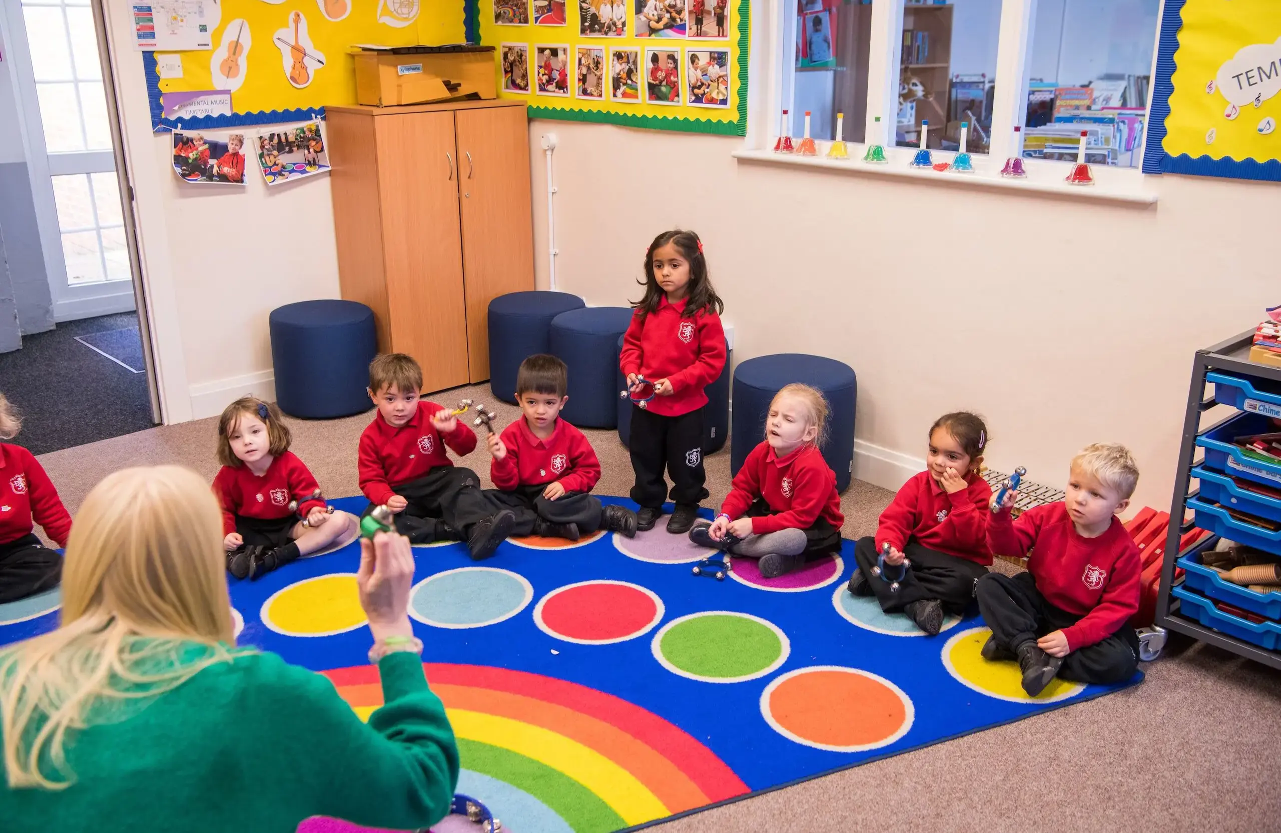 Children on a spotted carpet listening to a teacher