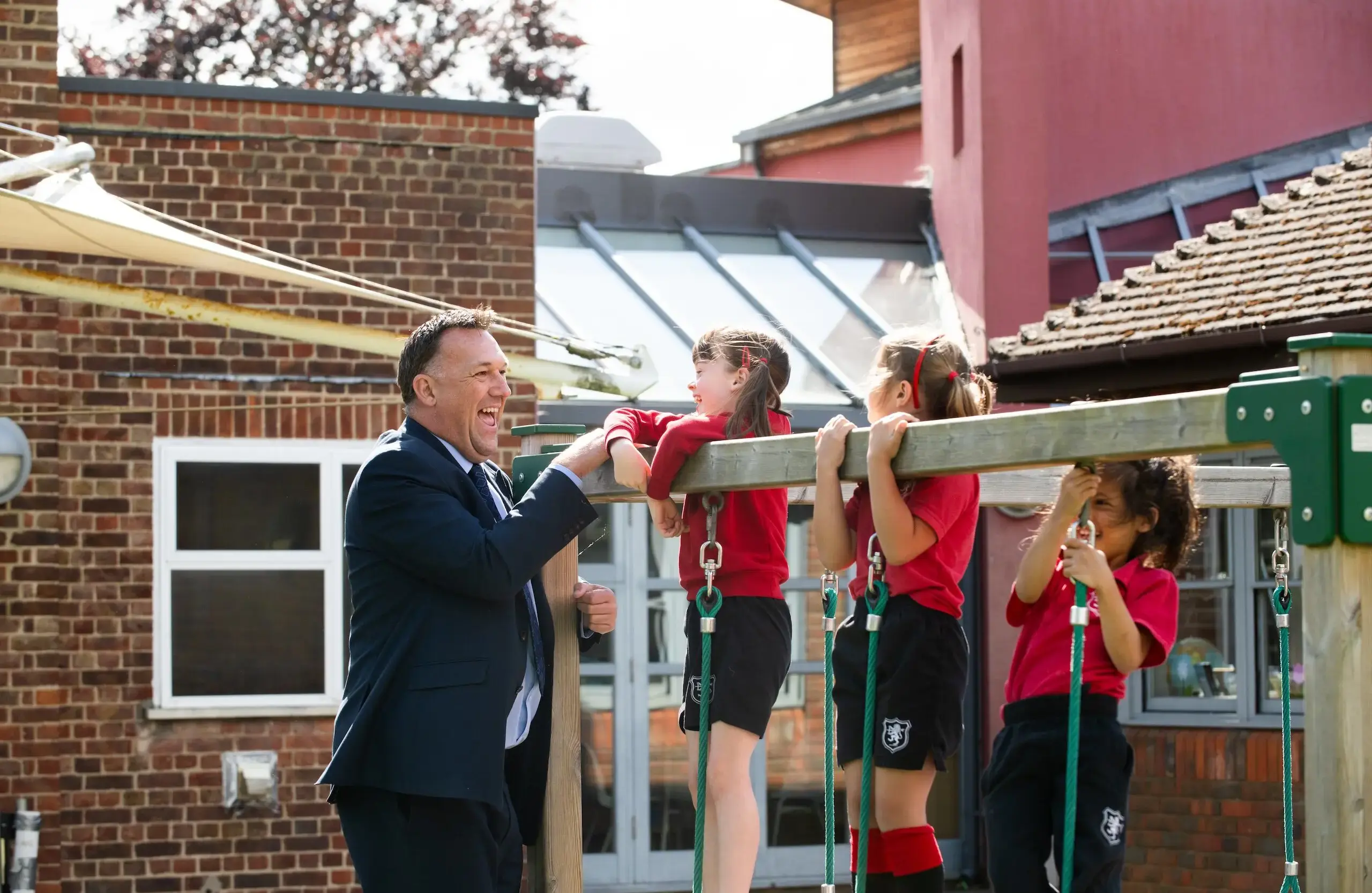 Teacher laughing with students as they play on playground equipment