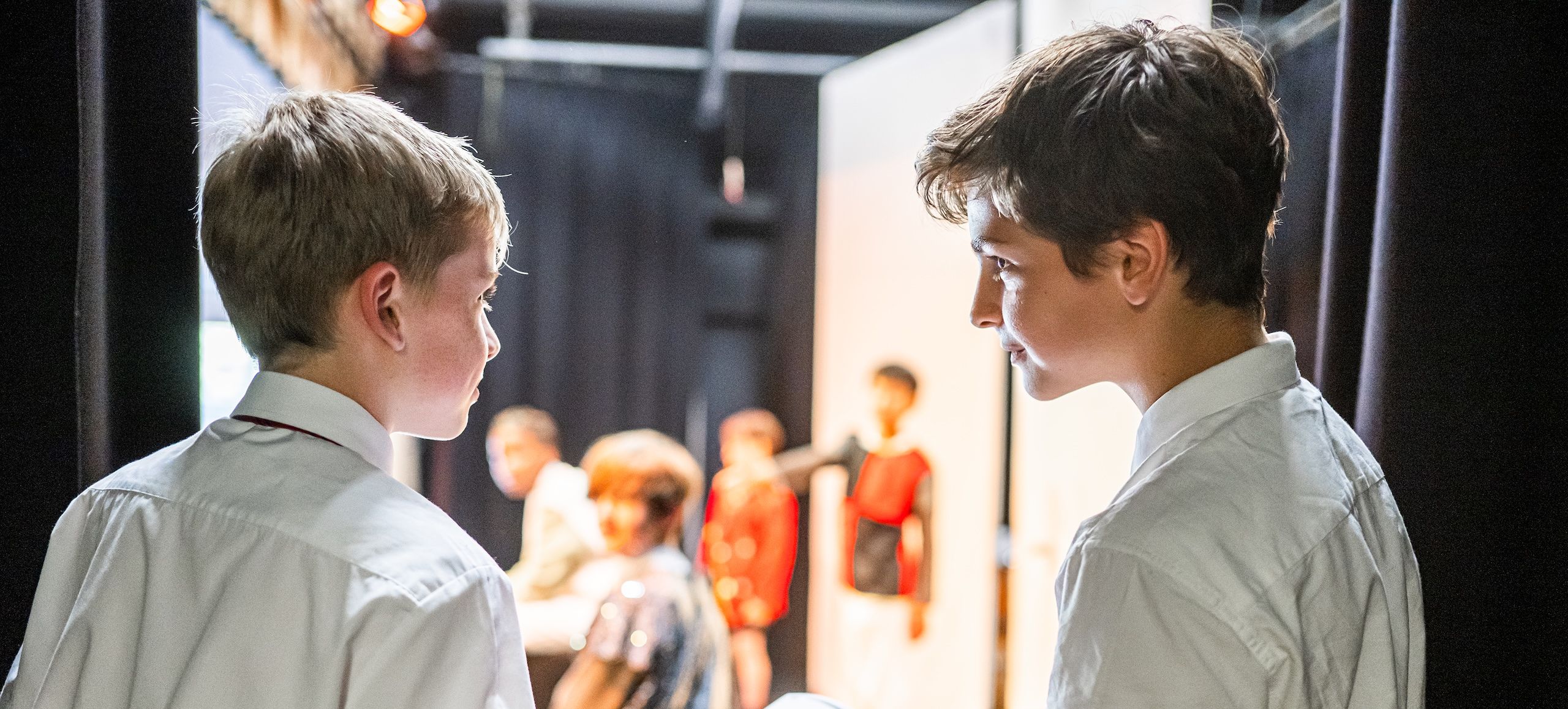 Two students speaking behind stage curtains with clipboard