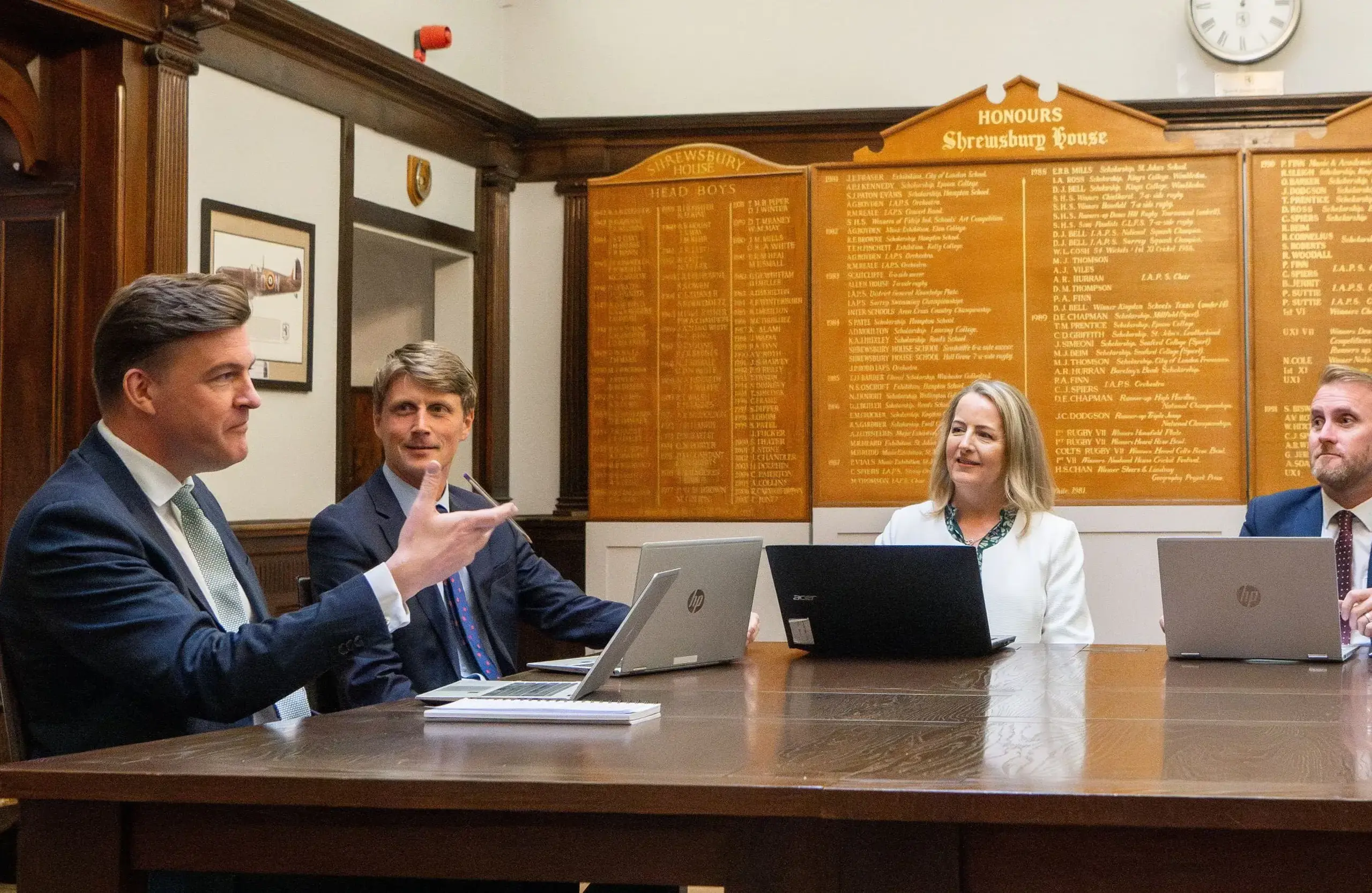 Four staff members in formal attire sitting at a table with laptops during a meeting.